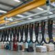 Overhead cable system in a factory with multiple black cables hanging from a yellow beam above a work area.